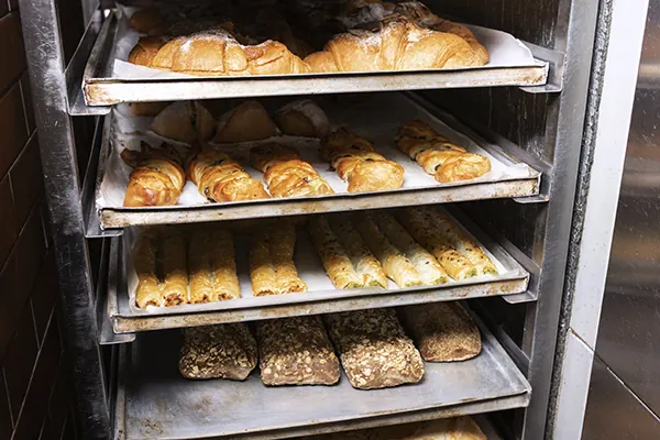 Assadeiras com pães saindo do forno de uma padaria.
