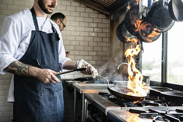 Cozinheiro trabalhando na chapa de uma cozinha profissional.